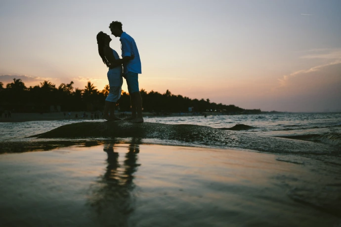 Couple silhouetted against a sunset on a beach.